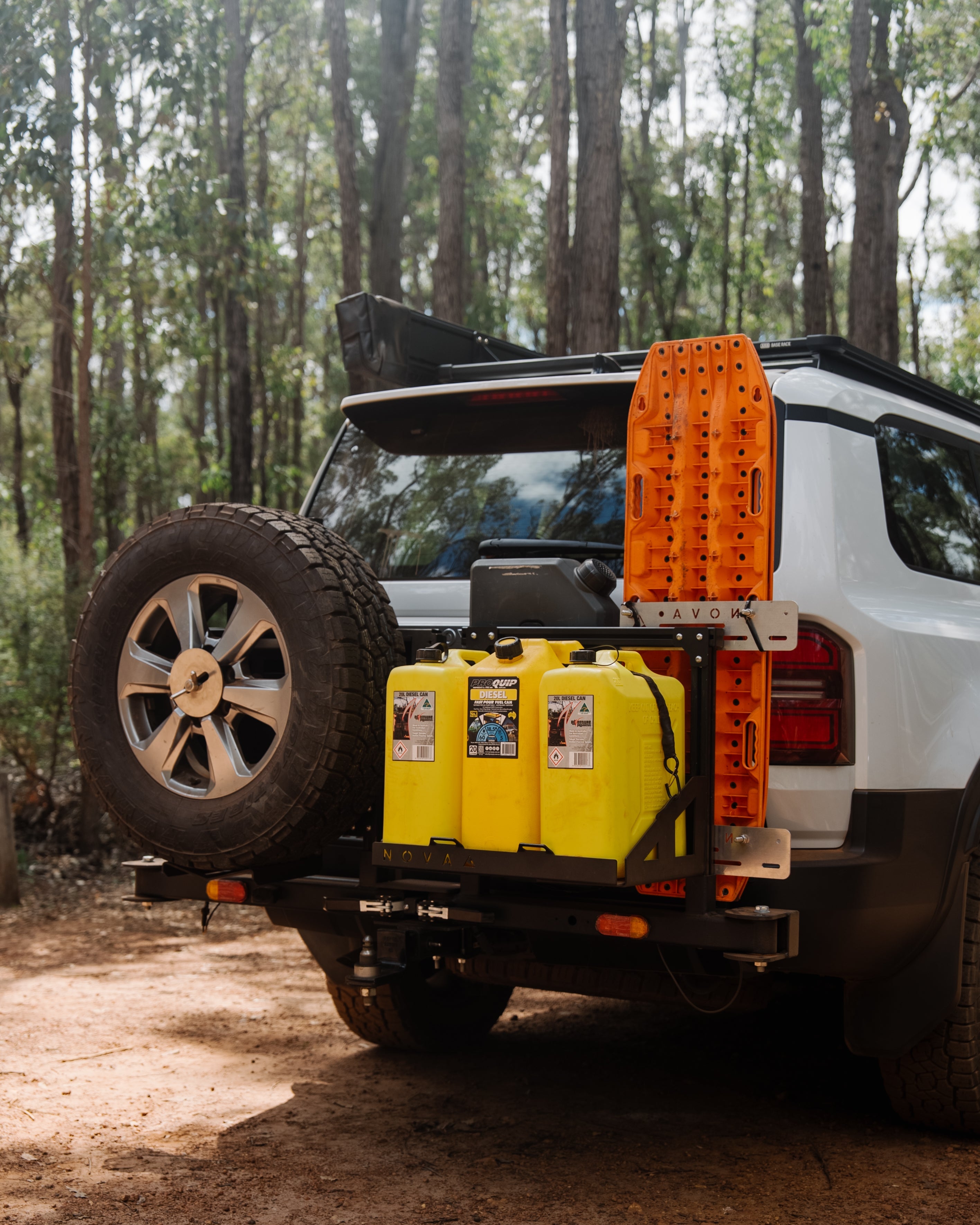 White SUV with yellow fuel cans and an orange toolbox on a dirt road in a forest.