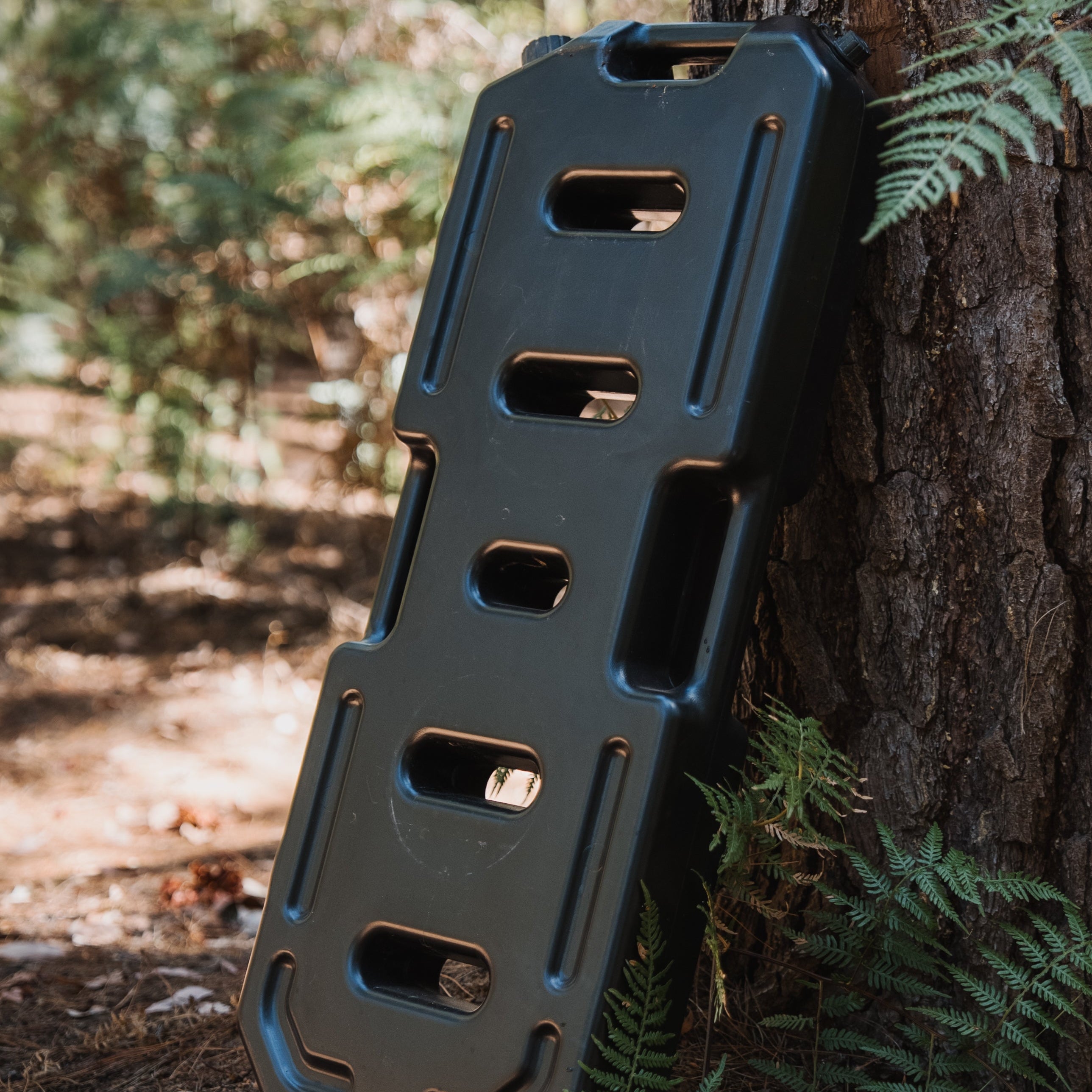 black water jerry can leaning against a tree in a forest setting