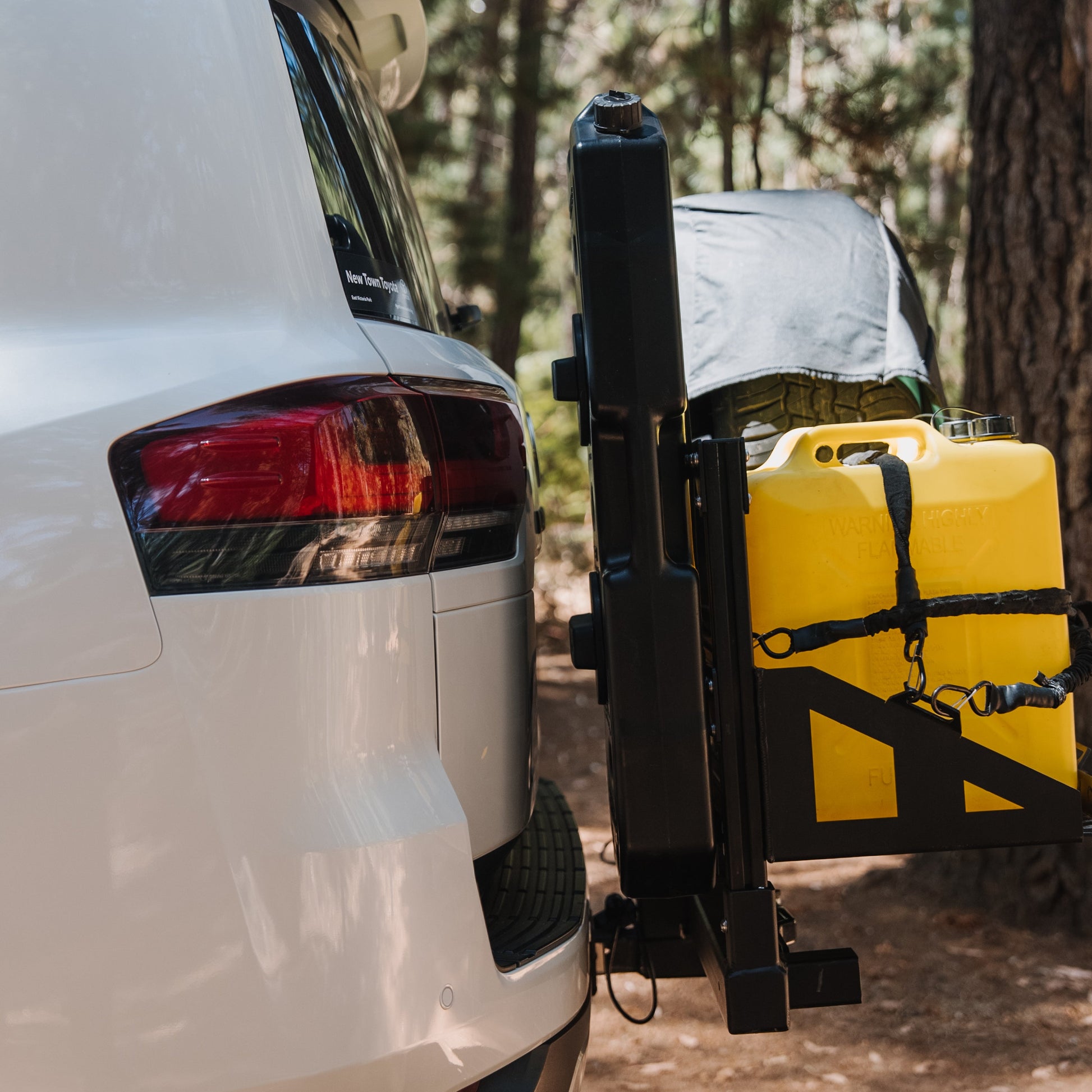White van with a yellow kayak on a trailer parked in a forest.