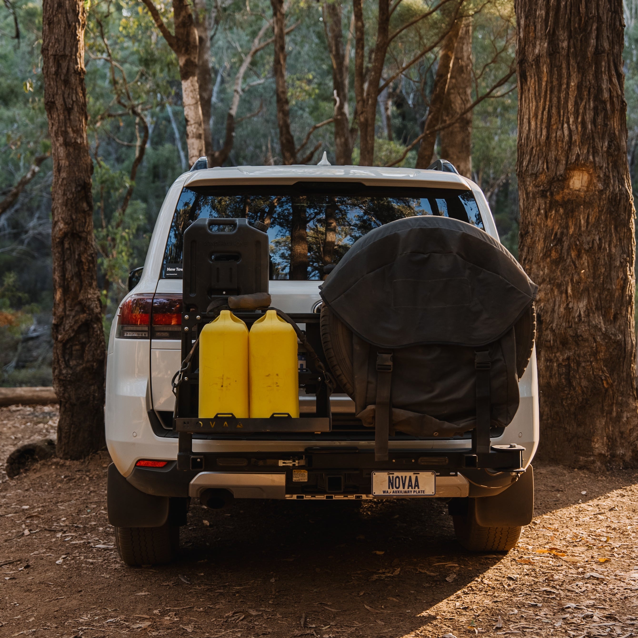 White SUV with yellow jerry cans in a forest setting