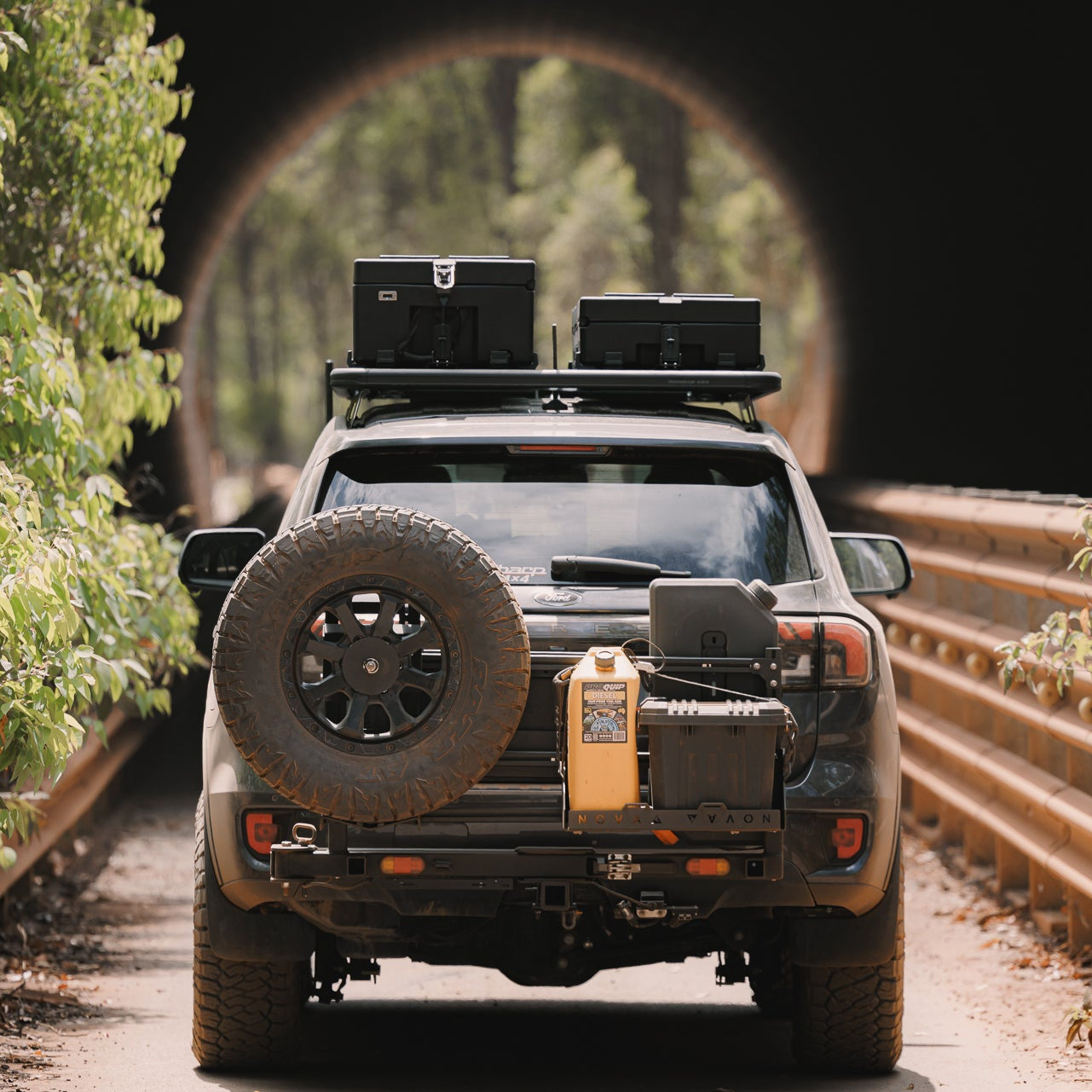 Off-road vehicle on a forest road with trees and guardrails.