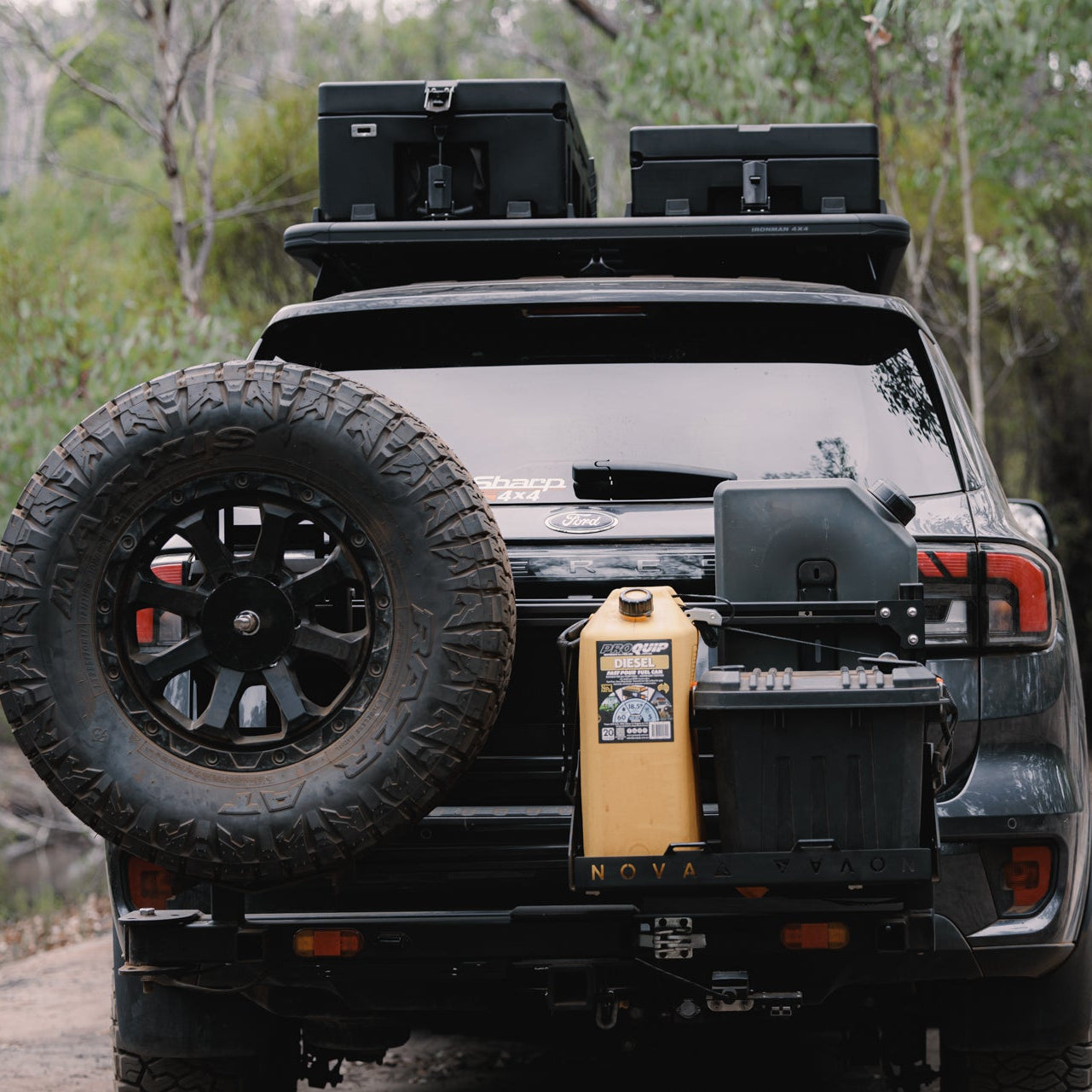 Black SUV with roof racks and a spare tire mounted on a forested trail